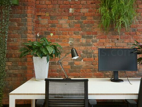 an office desk with two chairs and a computer on it, in front of a brick wall