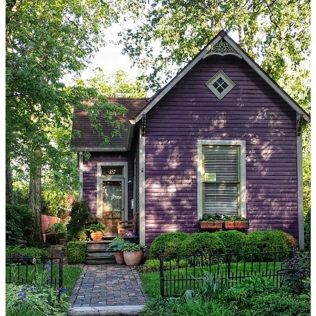 a purple house in the middle of some bushes and trees with potted plants on each side