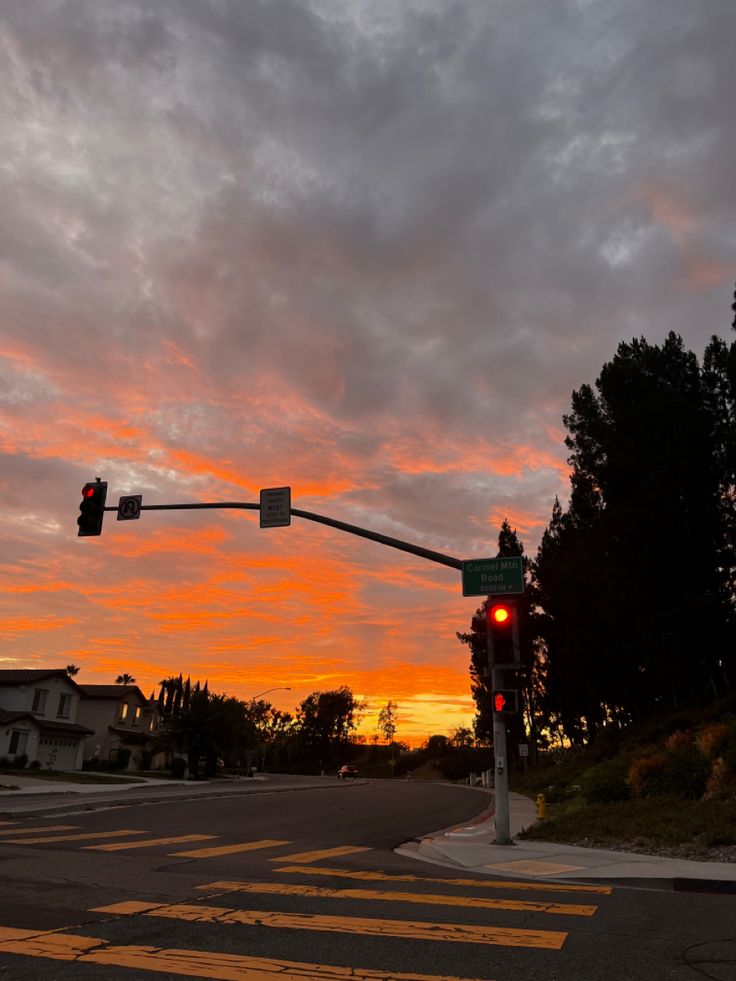 the sun is setting over an intersection with traffic lights and trees in the foreground