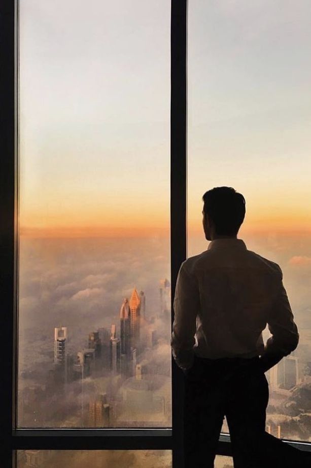 a man standing in front of a window looking out at the city below and skyscrapers