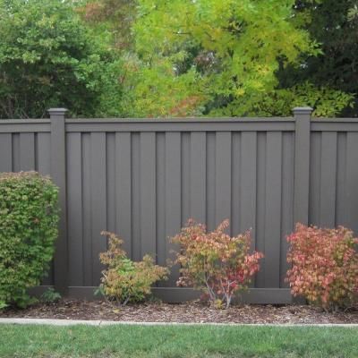 some bushes and trees in front of a gray fence with green grass on the other side