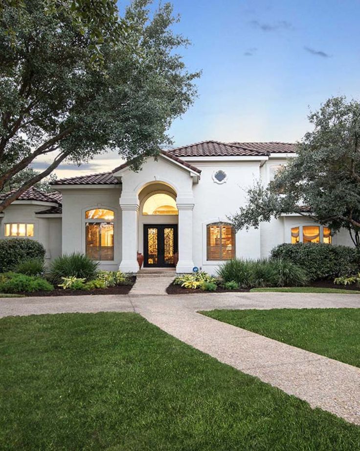 a white house with lots of windows and trees in front of the door is surrounded by lush green grass