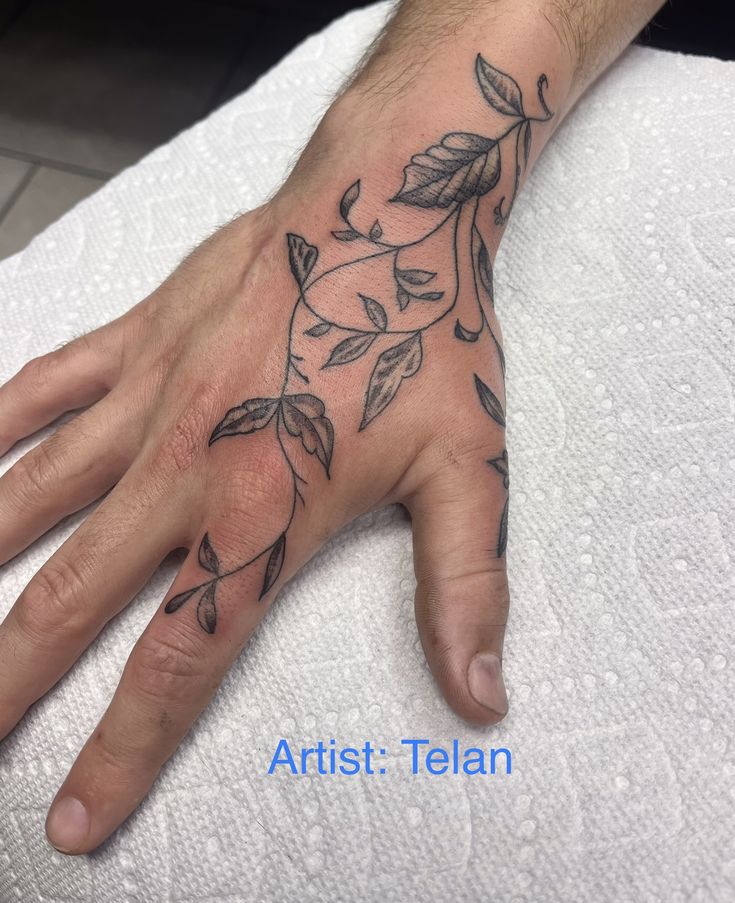 a person's hand on top of a towel with leaves and vines tattooed on it