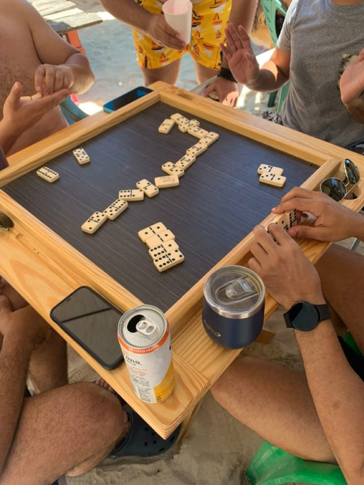 people playing domino board game on the beach with cans of beer and can openers