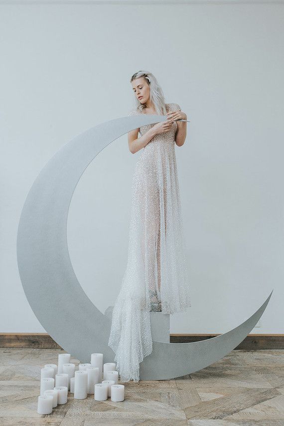 a woman in a white dress standing on top of a crescent shaped object with candles around her