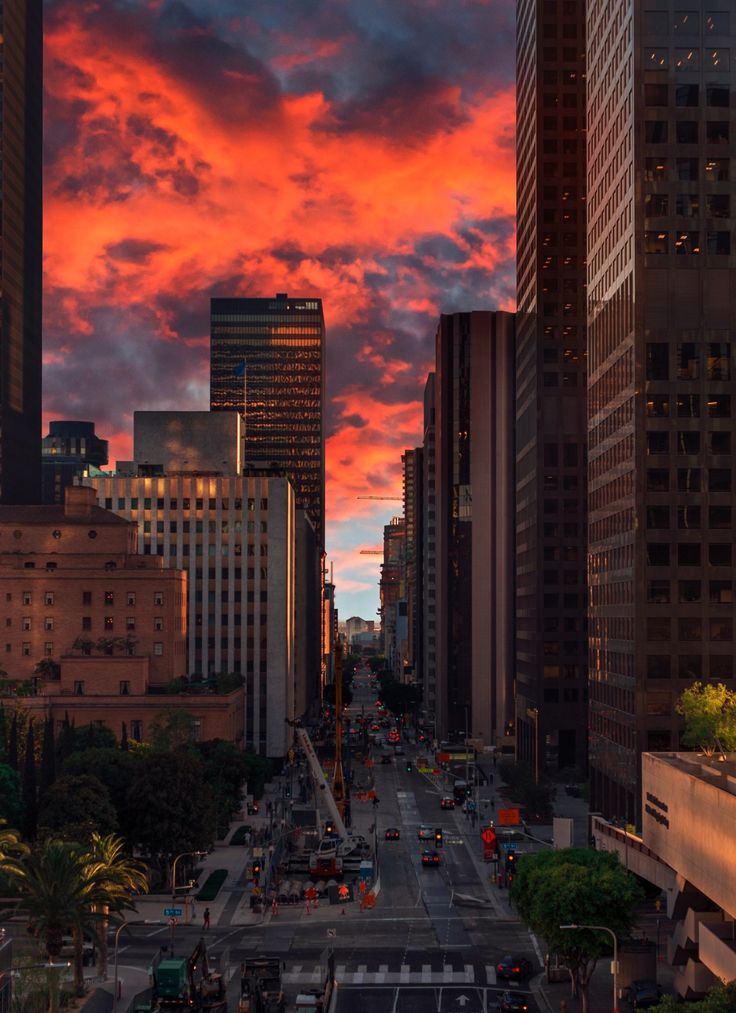 a city street with tall buildings and cars on it under a colorful sky at sunset