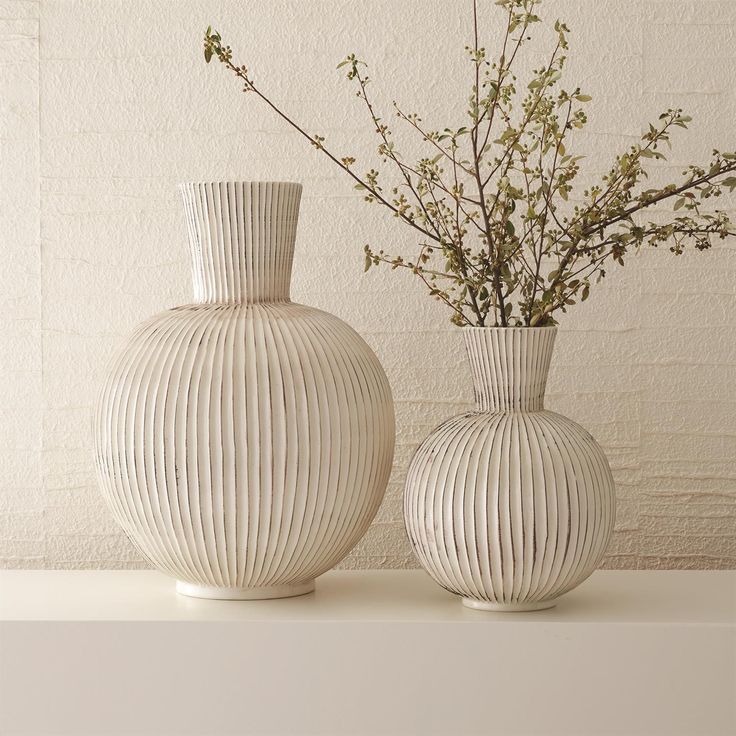 two white vases sitting next to each other on a shelf with flowers in them