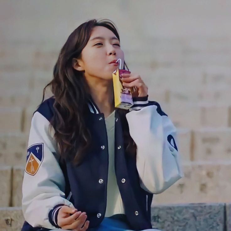 a young woman sitting on a bench holding a drink and eating something out of her hand