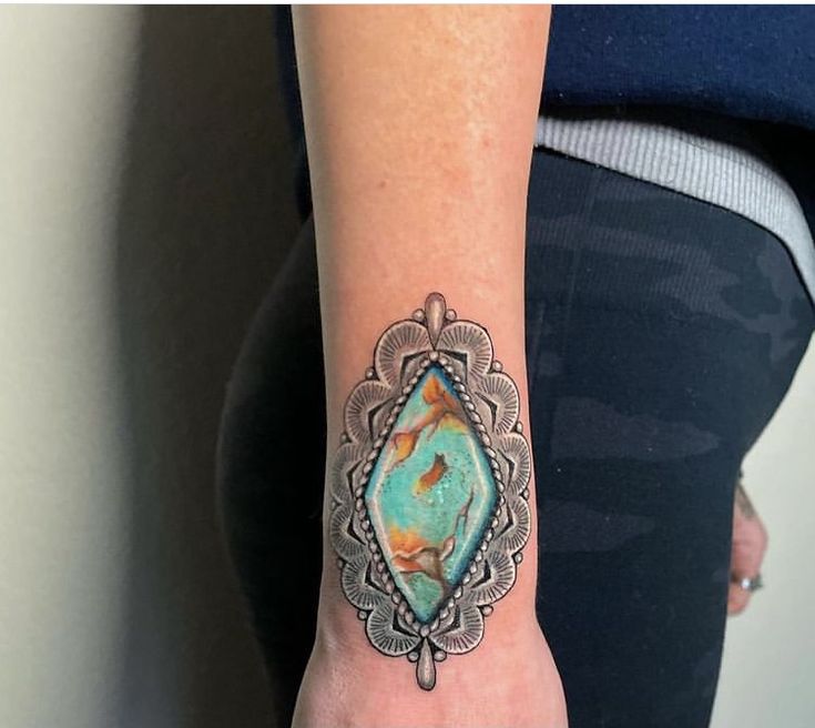 a woman's arm with a turquoise stone tattoo on it