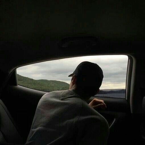 a man sitting in the passenger seat of a car looking out the window at mountains