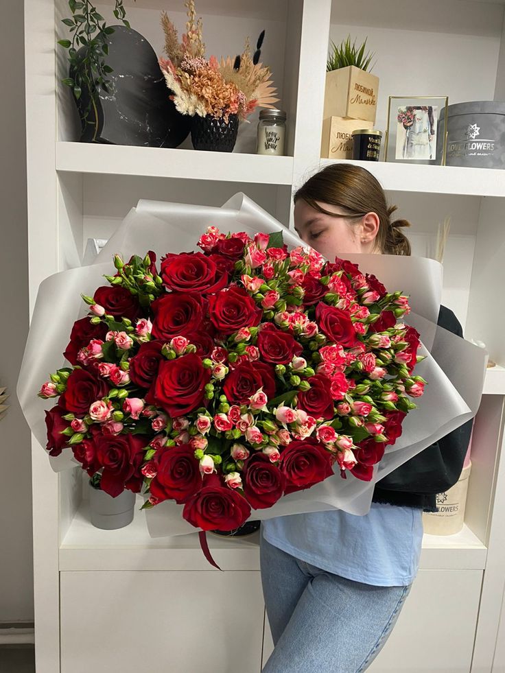 a woman holding a large bouquet of red roses in front of a white bookcase