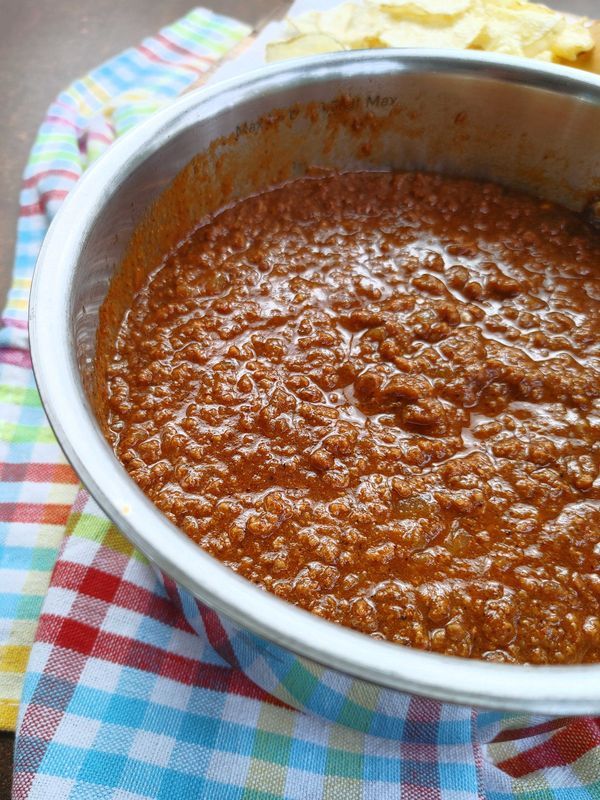 a bowl filled with chili on top of a checkered table cloth next to chips