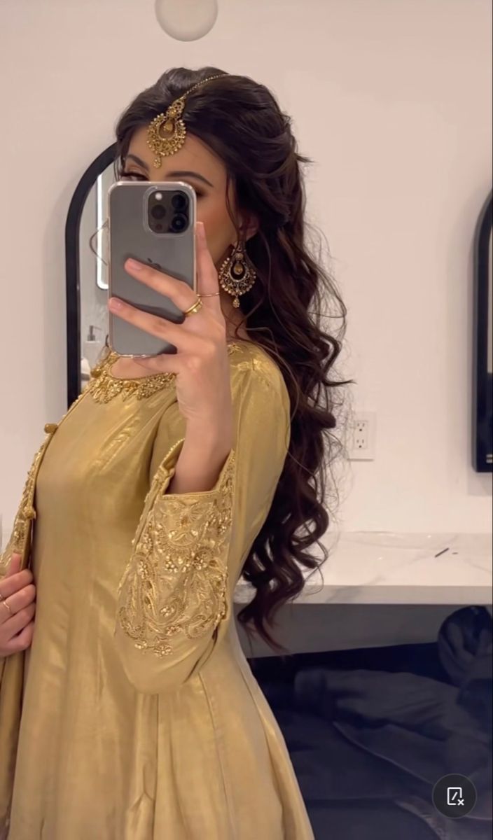 a woman taking a selfie in front of a mirror wearing a gold dress and headpiece