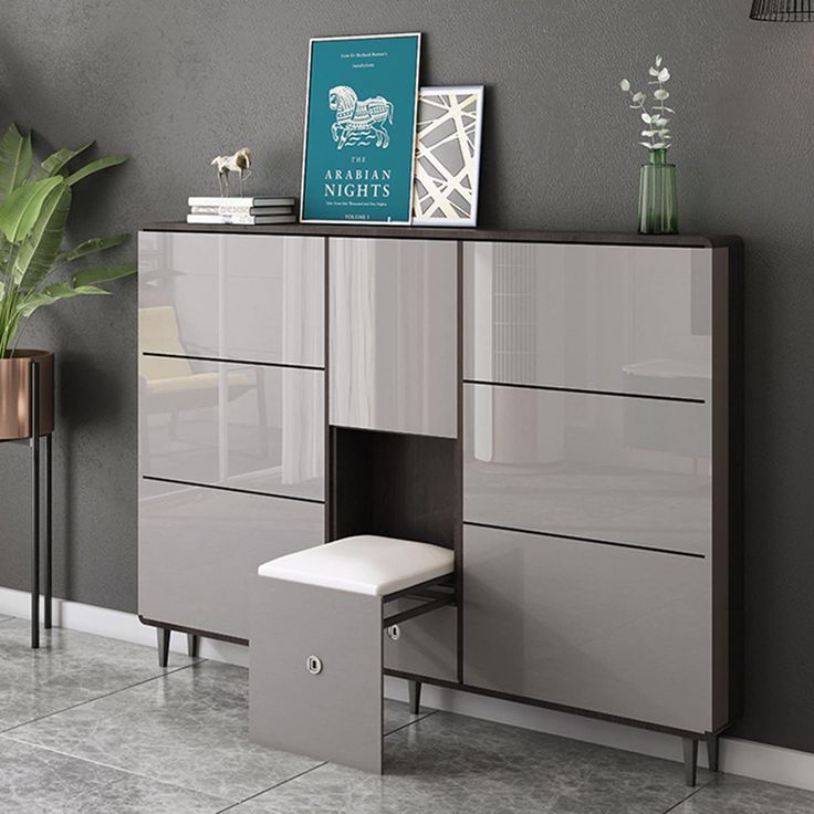 a modern dresser with two drawers and a stool in the corner next to it, against a gray wall