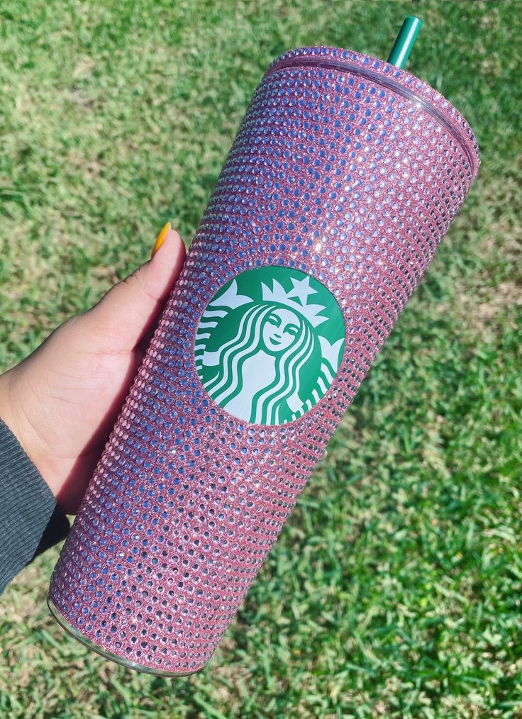 a hand holding a purple starbucks cup in the grass