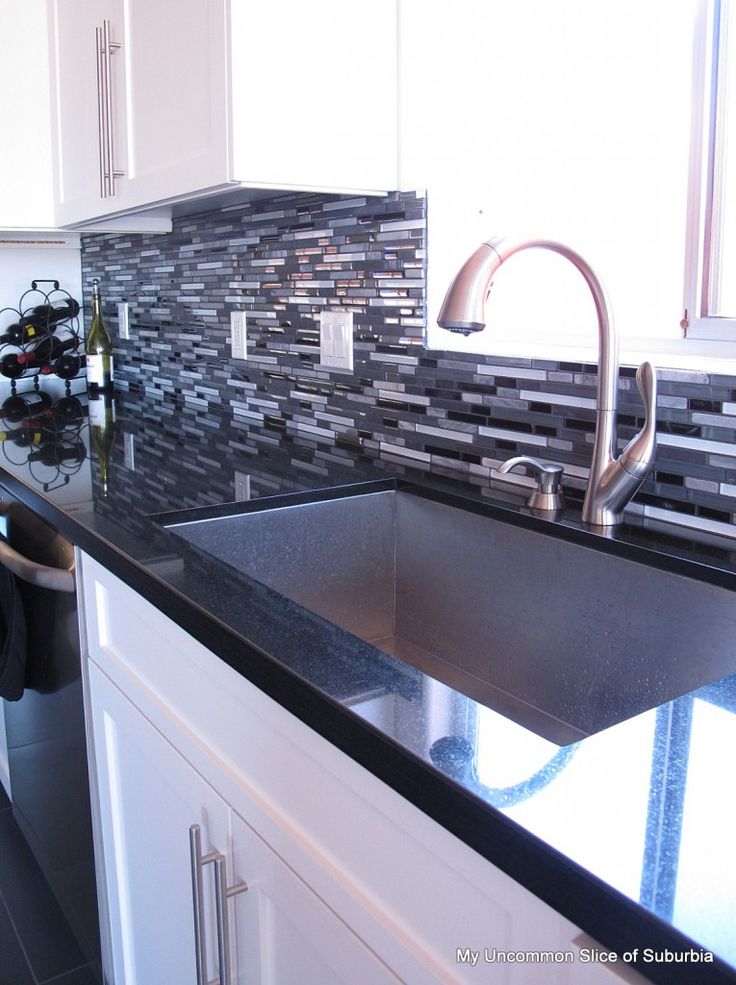 a kitchen sink sitting under a faucet next to a counter top with a bottle of wine on it