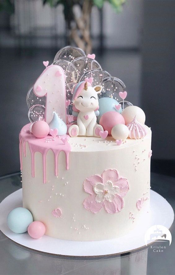 a white cake with pink icing and an unicorn figure on top is sitting on a table