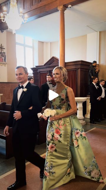 a man and woman in formal wear walking down the aisle at a wedding ceremony with other people behind them