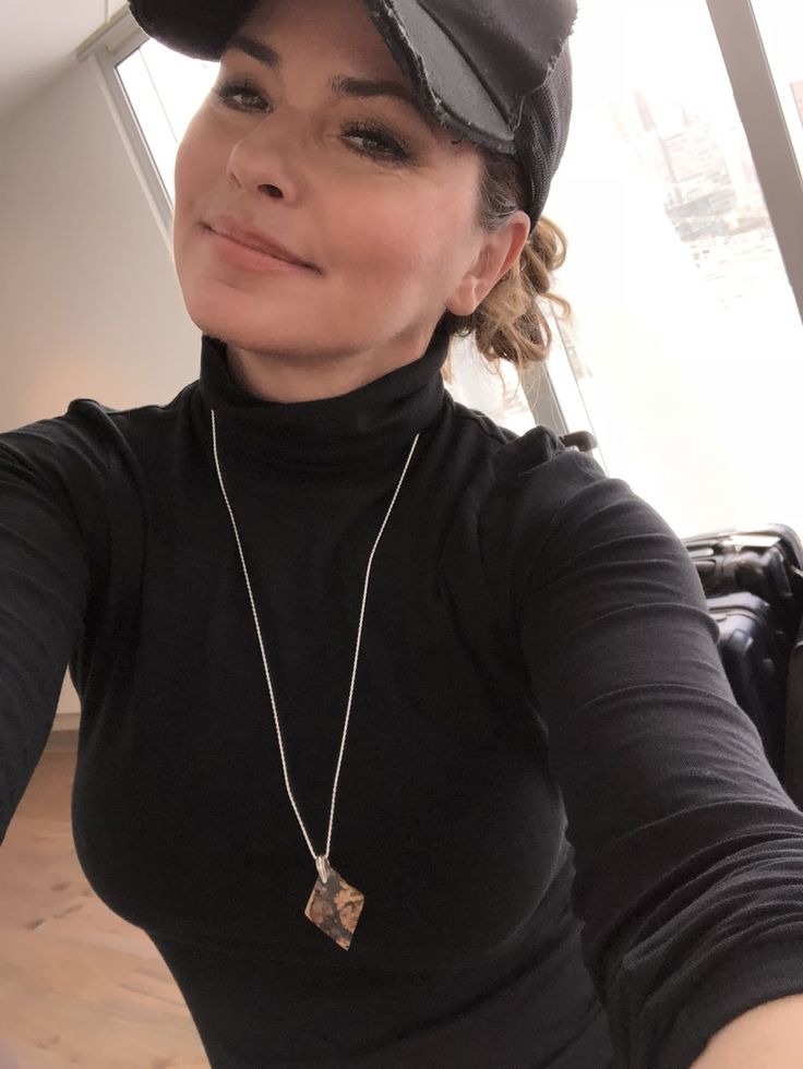 a woman taking a selfie in front of a window wearing a black shirt and hat