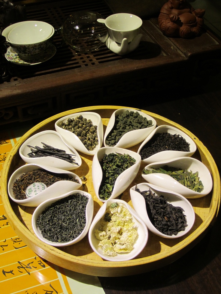 several spoons filled with different kinds of tea on a tray next to cups and saucers