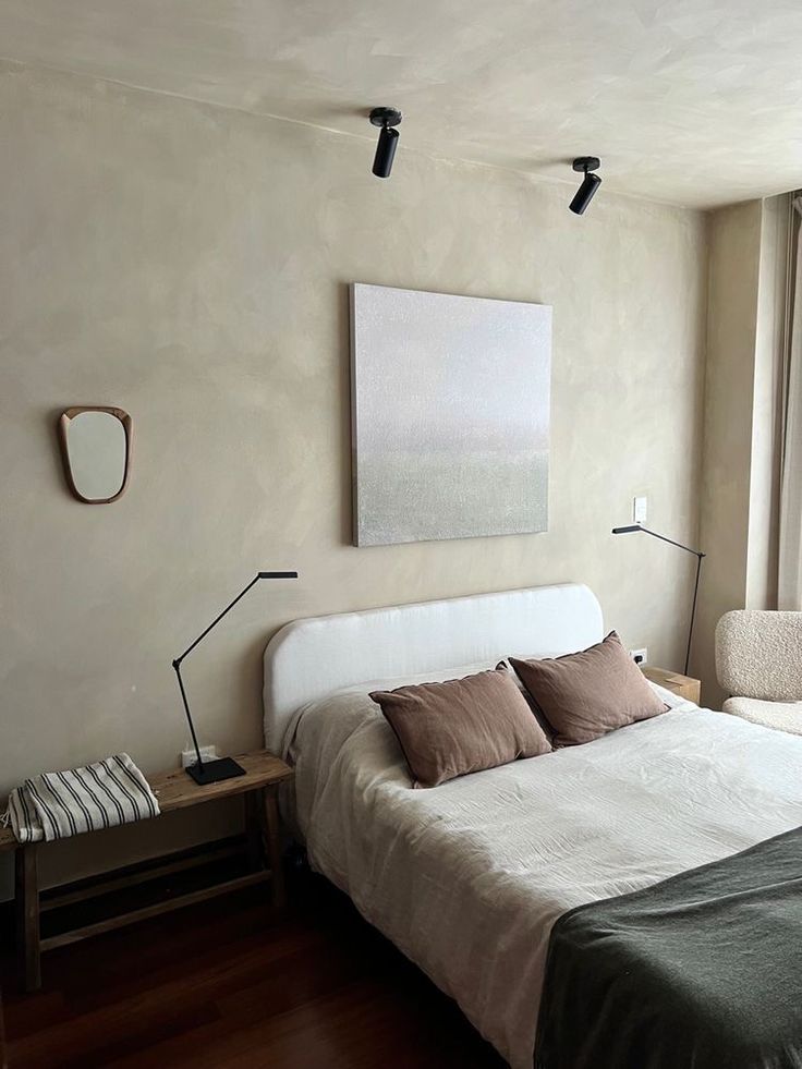 a bed sitting in a bedroom next to a window with a painting on the wall