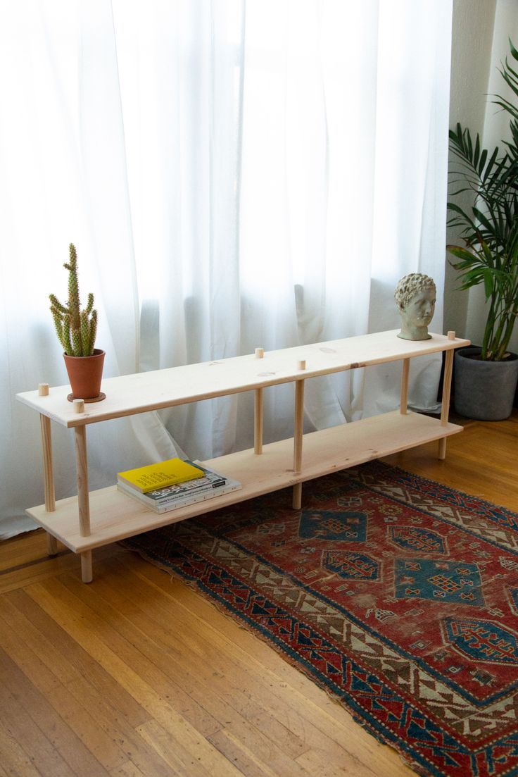 a wooden shelf sitting on top of a hard wood floor next to a potted plant