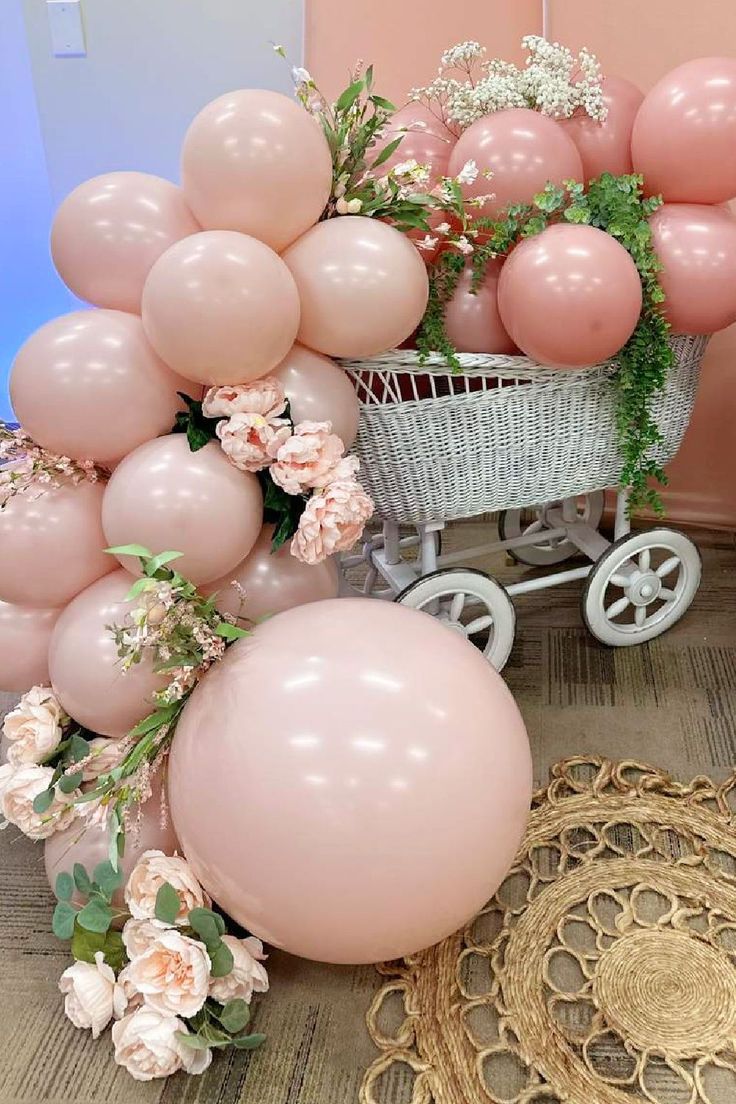 a baby carriage filled with pink balloons and greenery next to a bunch of flowers