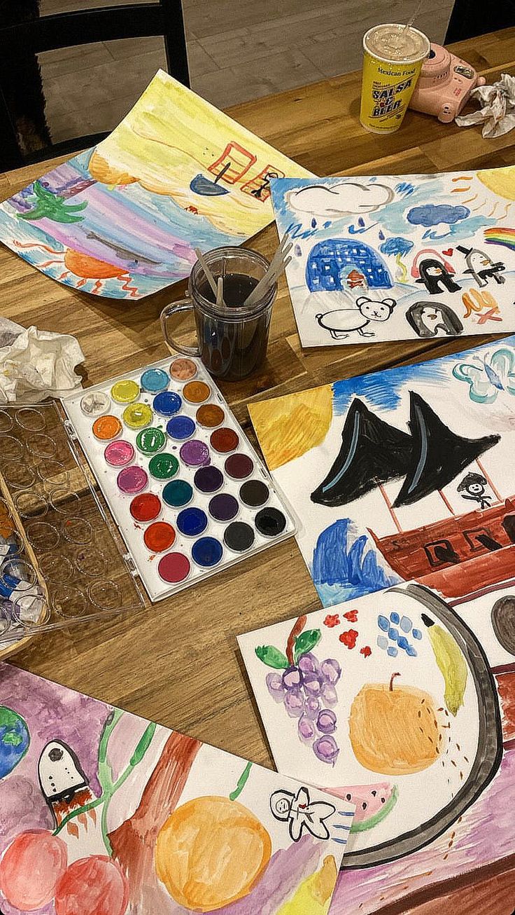 children's art work is displayed on the table with their paintings and watercolors