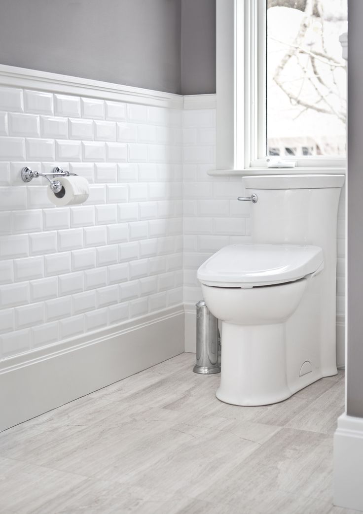 a white toilet sitting next to a window in a bathroom on top of a hard wood floor