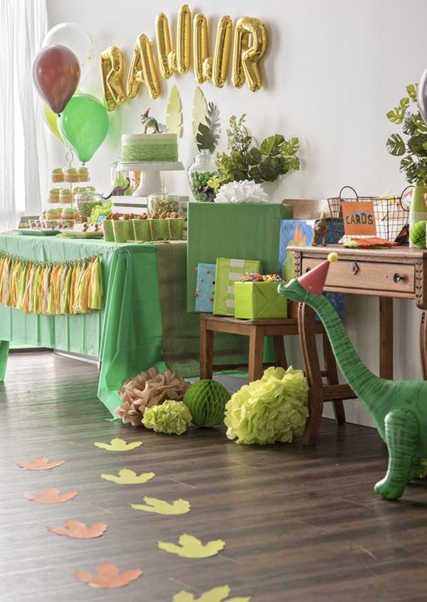 a dinosaur birthday party with balloons, streamers and paper leaves on the floor in front of it