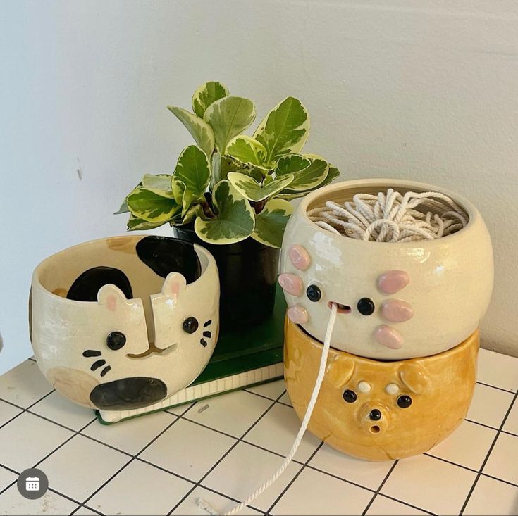 two planters that have faces on them sitting on a tiled counter next to a potted plant