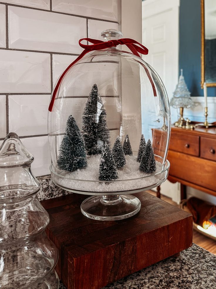 a glass bowl filled with snow covered trees on top of a wooden table next to a mirror