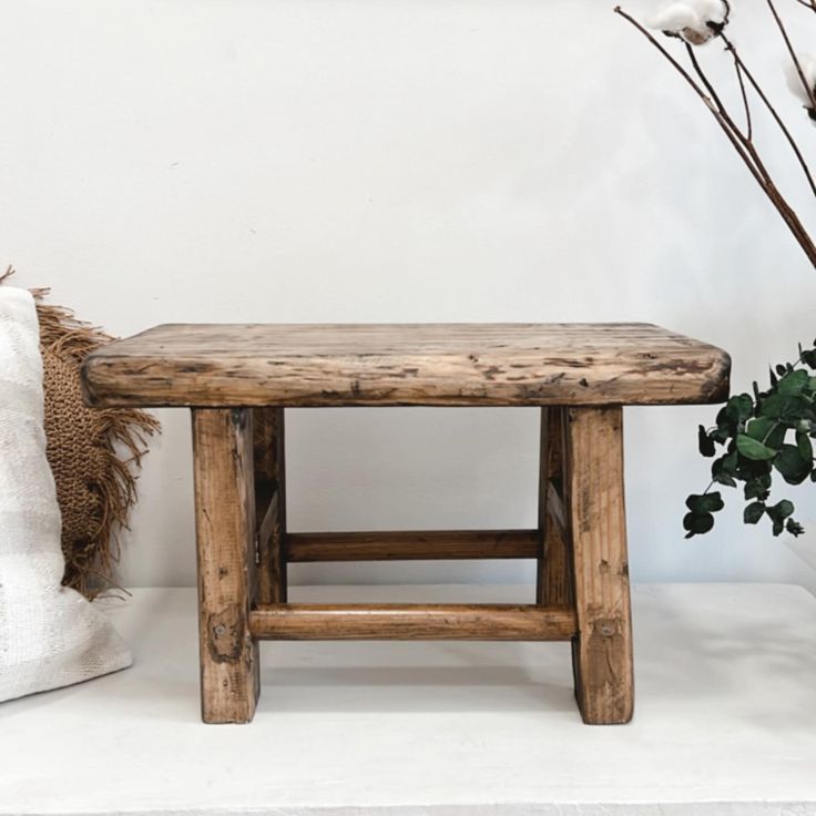 a wooden bench sitting next to a potted plant on top of a white table