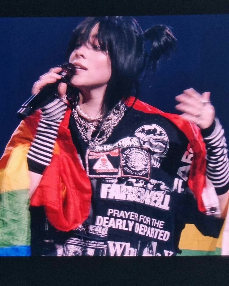 a woman with black hair holding a microphone in her right hand and wearing a colorful shirt