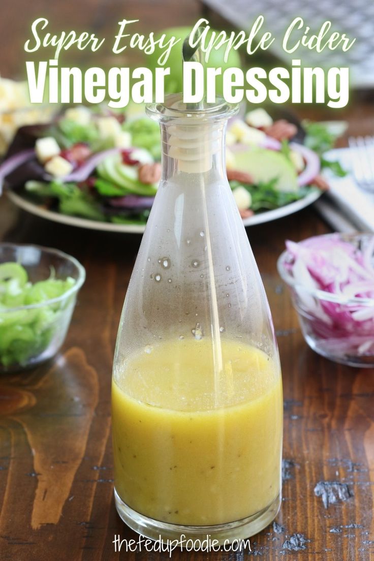 a bottle filled with dressing sitting on top of a wooden table next to plates of salad