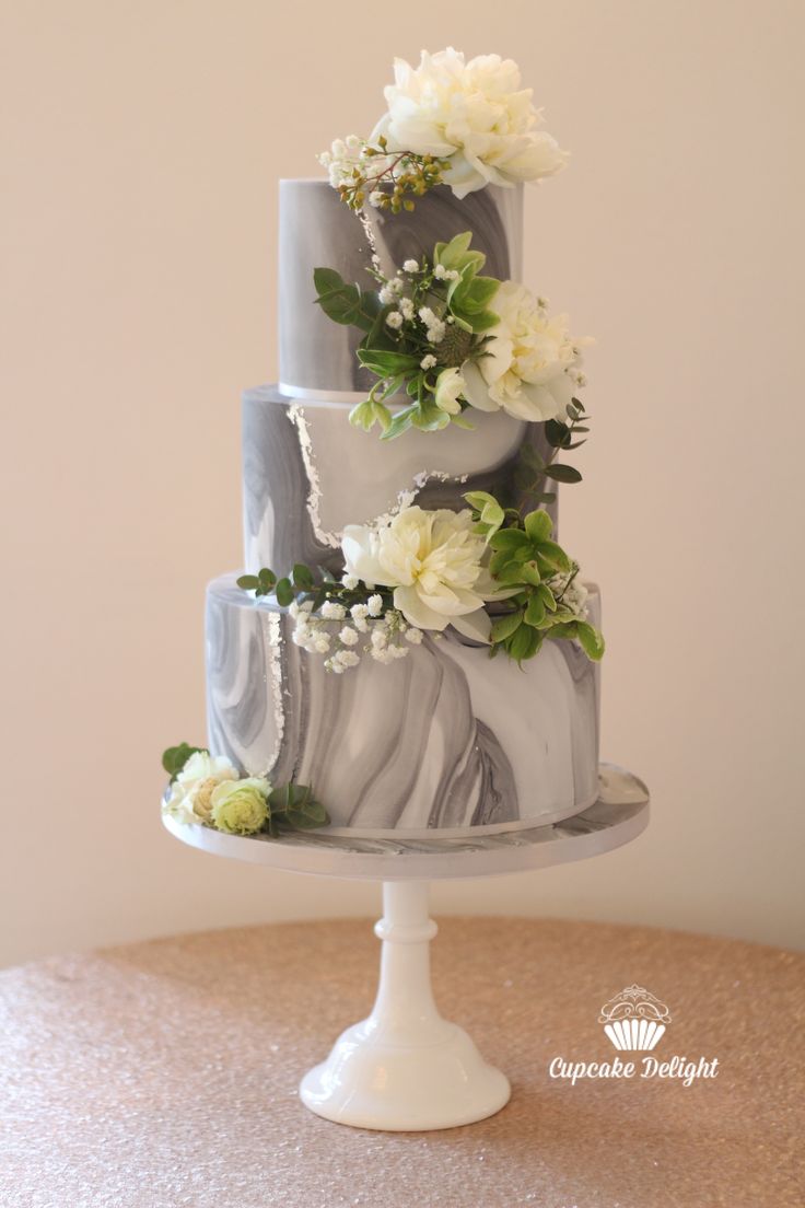 a marbled three tiered cake with white flowers on the top and green leaves