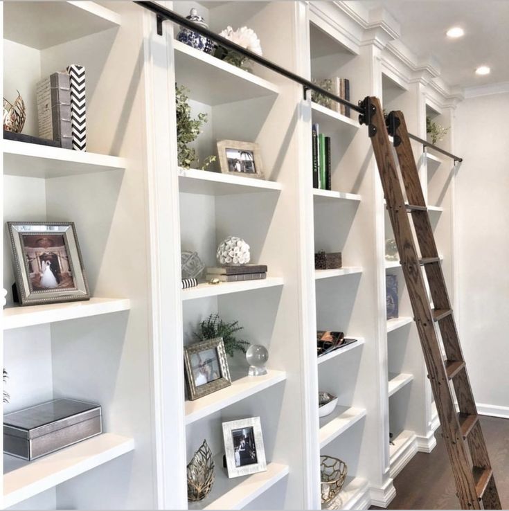 a ladder leaning up against a white bookshelf filled with lots of shelves and pictures