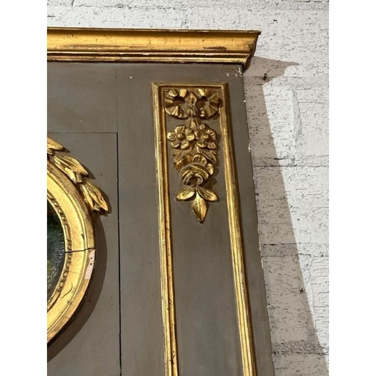 an ornate gold framed mirror on the side of a white brick wall next to a gray door