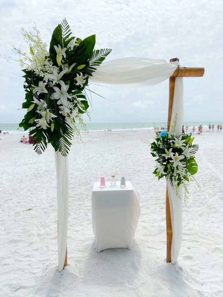 an outdoor wedding setup on the beach with white flowers and greenery at the altar