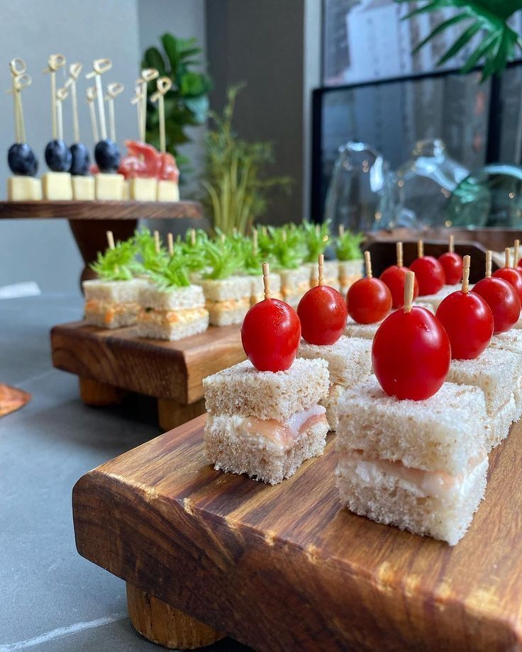 small sandwiches with tomatoes and lettuce on wooden trays next to other food items