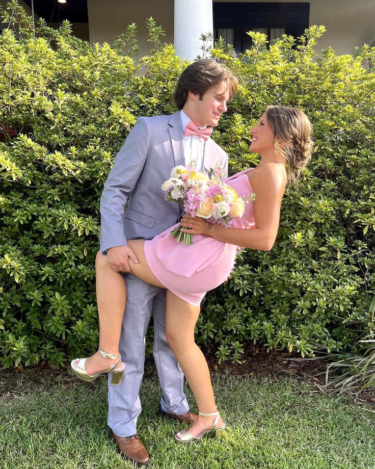 a man in a tuxedo holding a woman in a pink dress and heels