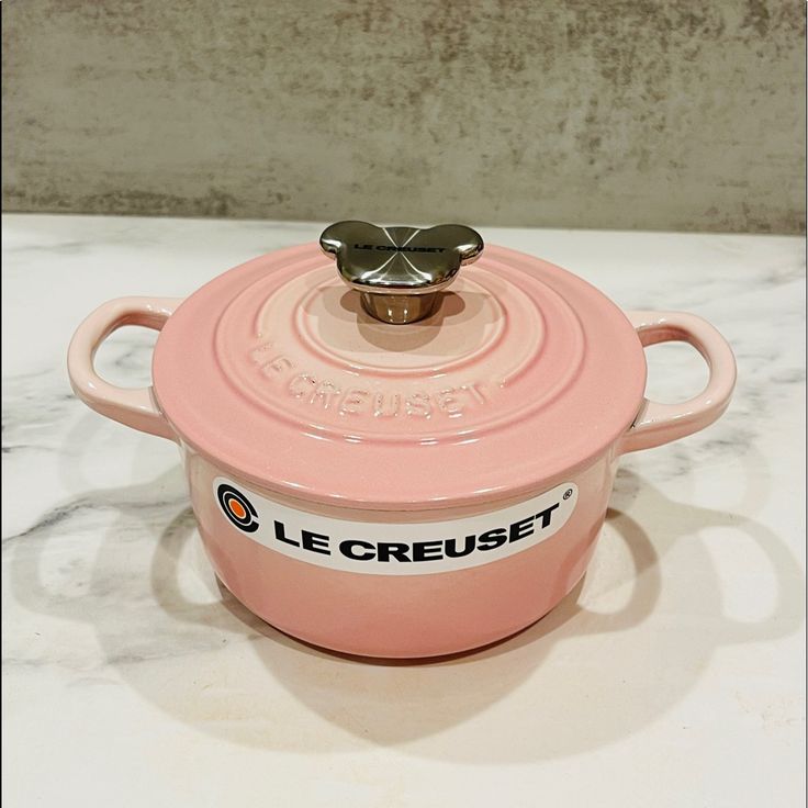 a pink casserole with a metal lid sitting on a marble countertop next to a wall