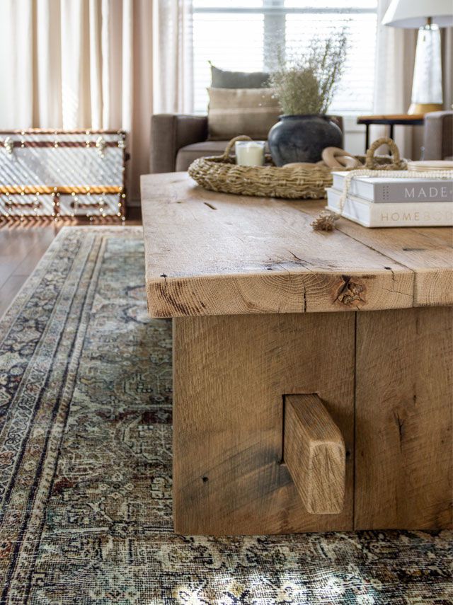 a living room with a large rug and wooden table in the centerpiece, next to a couch