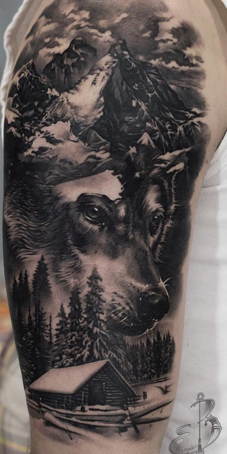 a man's arm with a wolf and mountain scene tattoo on the upper half