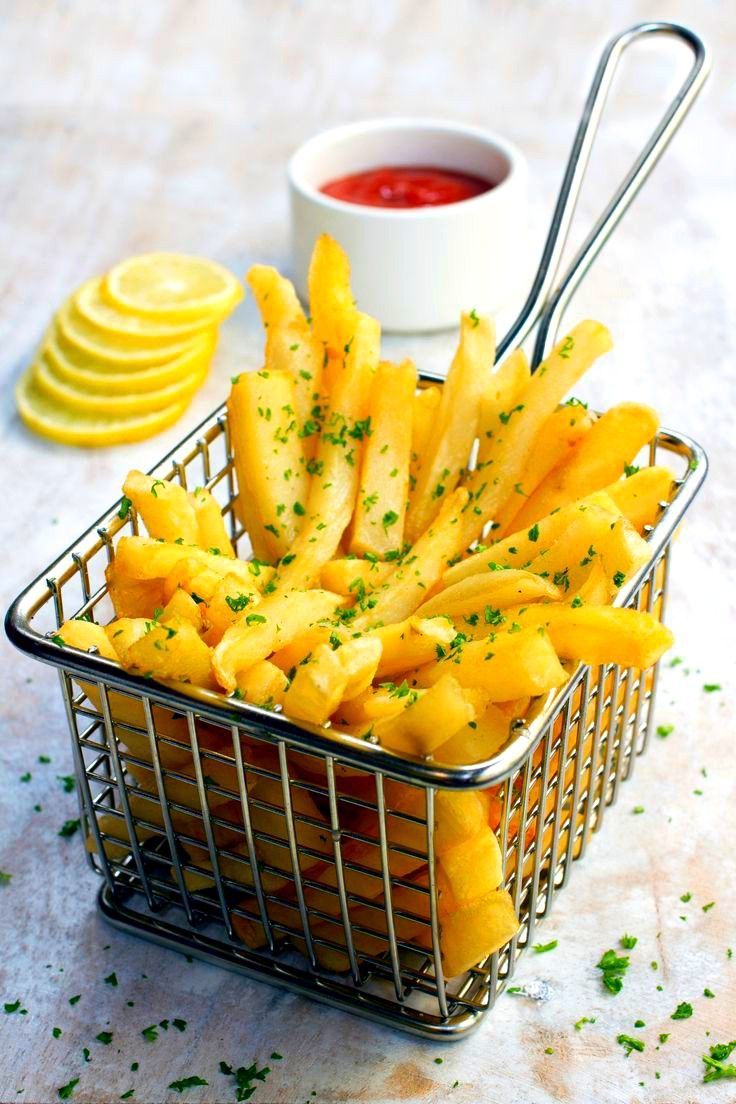 a metal basket filled with fries next to a bowl of ketchup and lemon wedges