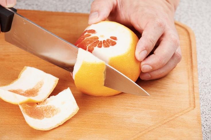 a person cutting an orange with a knife on a cutting board next to some cut up pieces