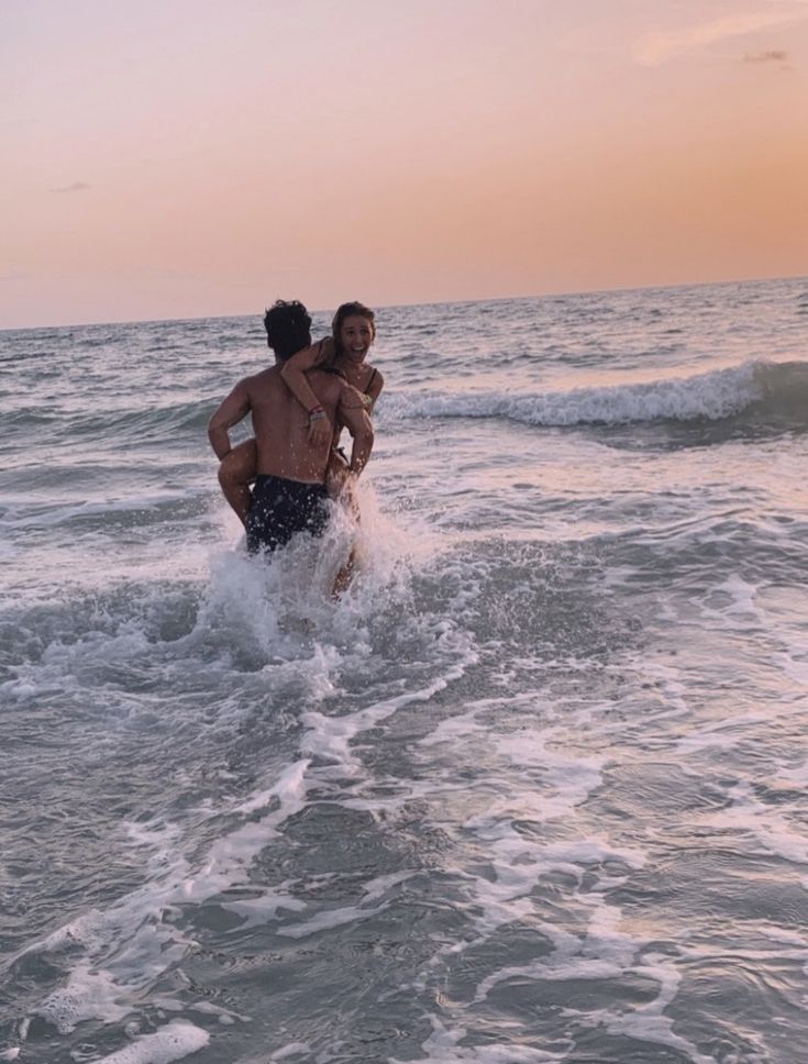 two people are playing in the water at sunset or dawn, one is carrying another man on his back