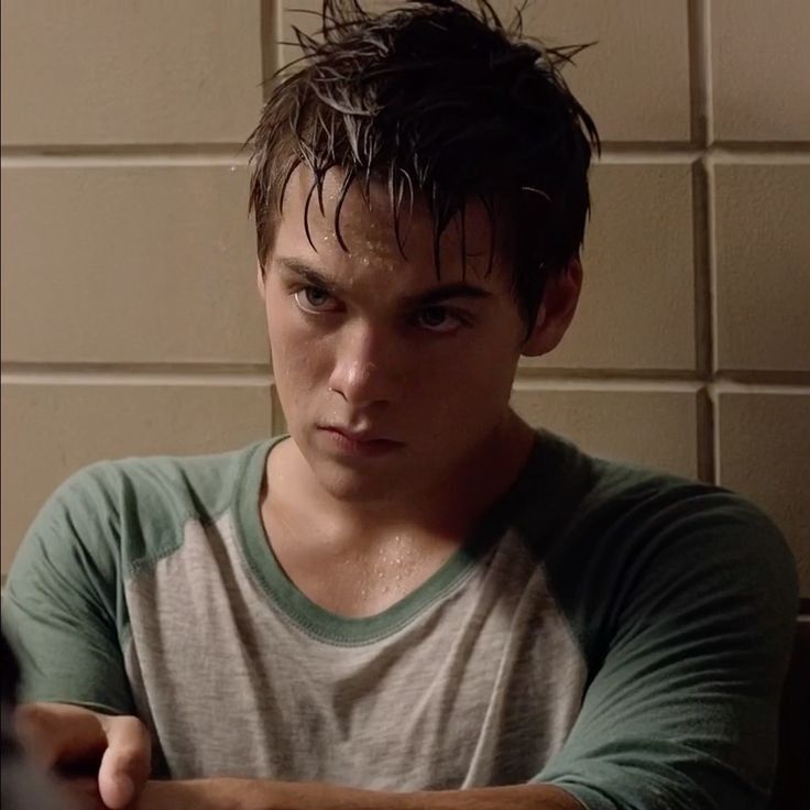 a young man sitting in front of a white wall with his hand on the keyboard