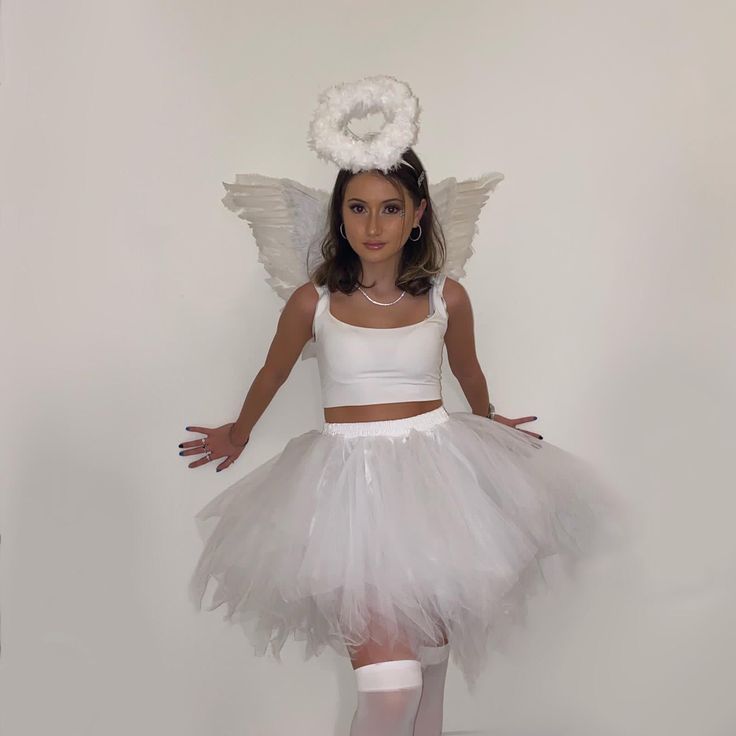 a woman in a white dress with angel wings on her head and arms, posing for the camera