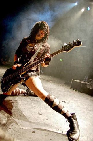 a woman with long hair and boots holding a guitar in front of a stage light